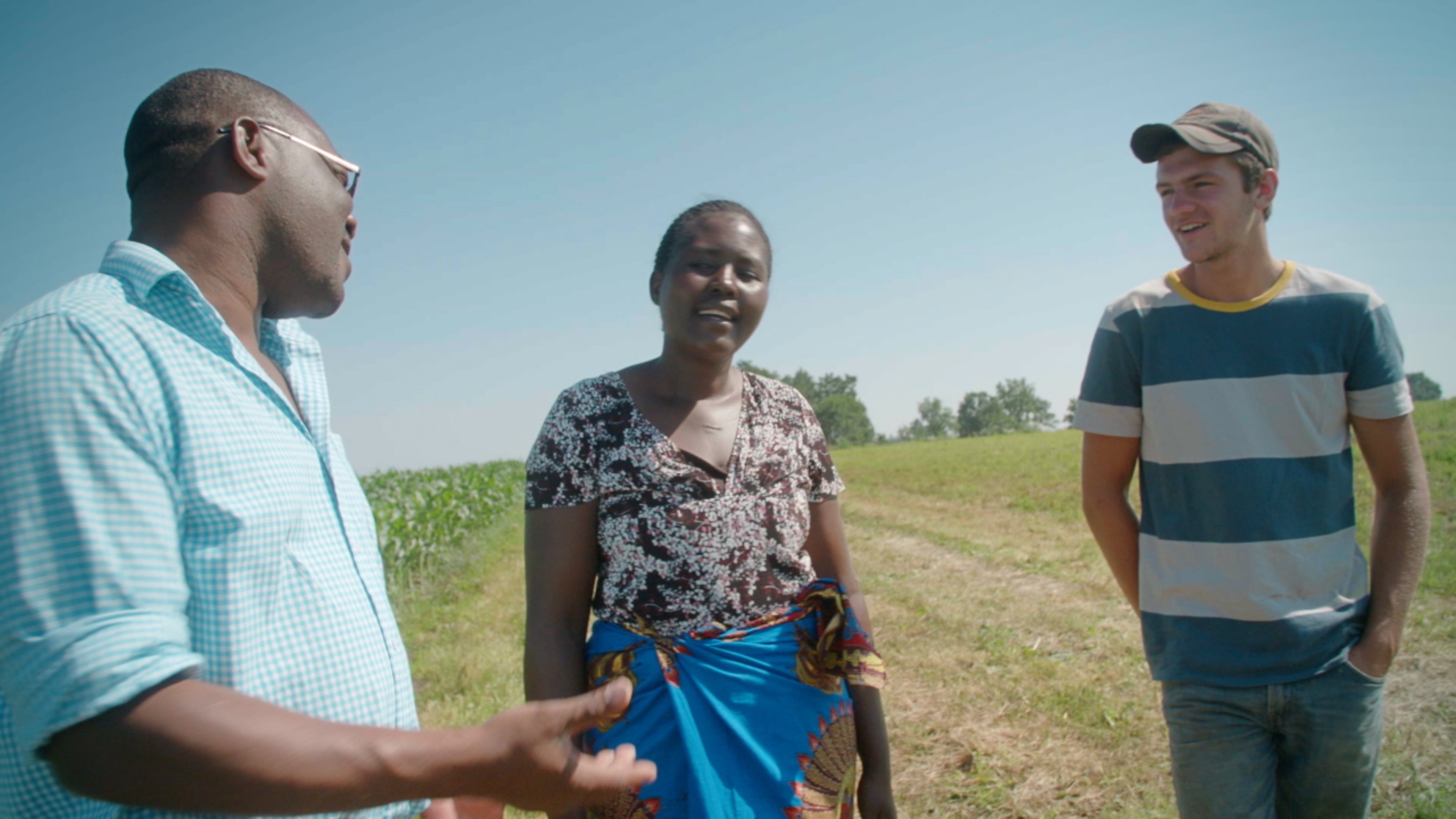 Three people stood talking in a field. A man on the left gestures with his hand towards the woman and young man stood beside him.