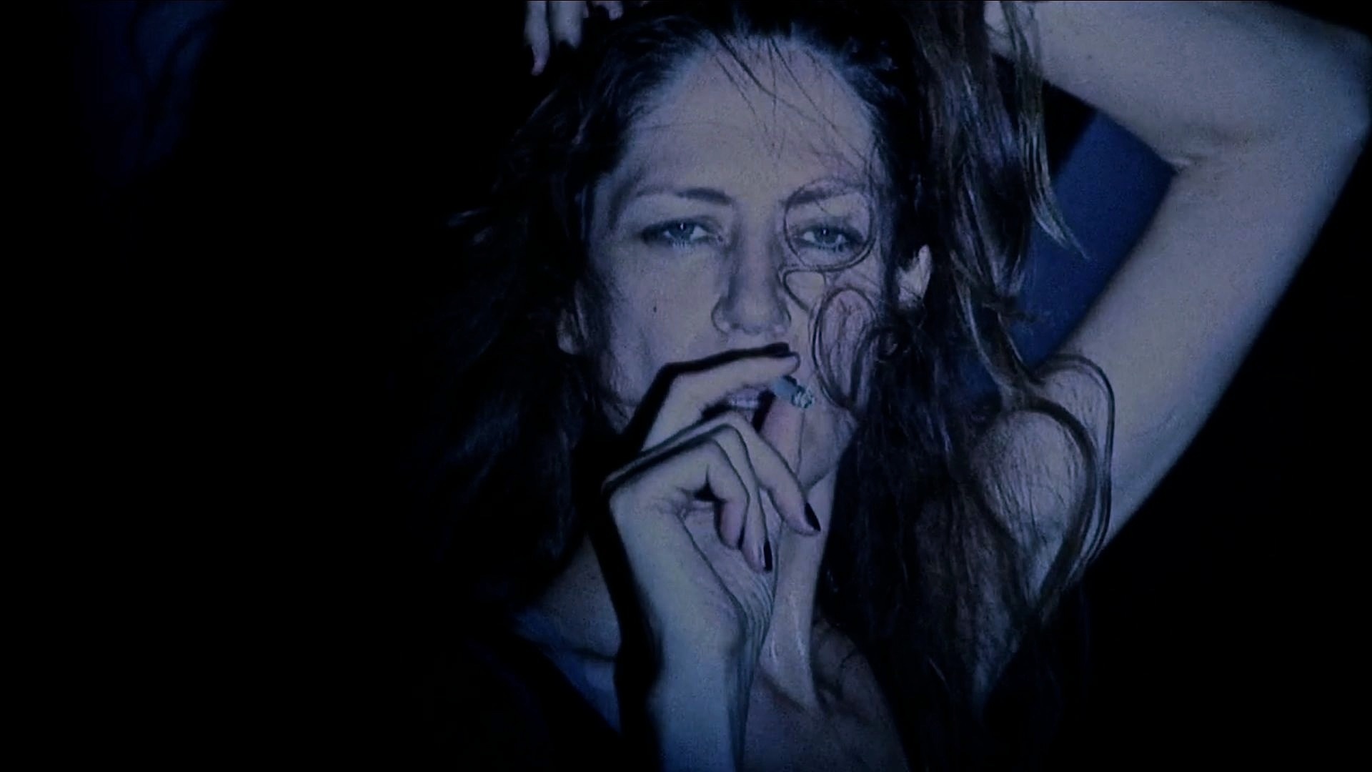 Shot of a woman smoking a cigarette. Her hair is swept across half of her face.