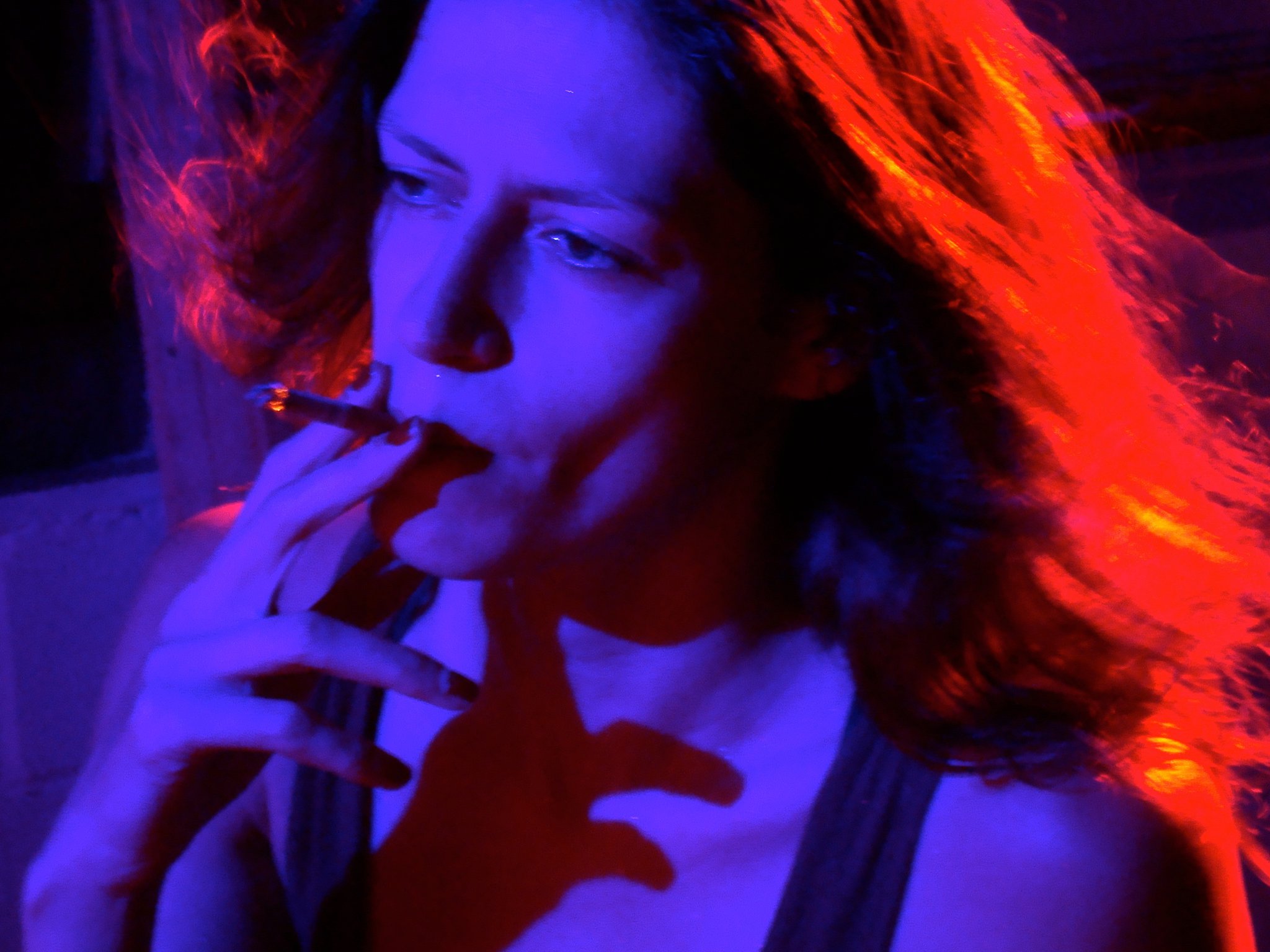 A woman smoking a cigarette. She's lit by a purple light.