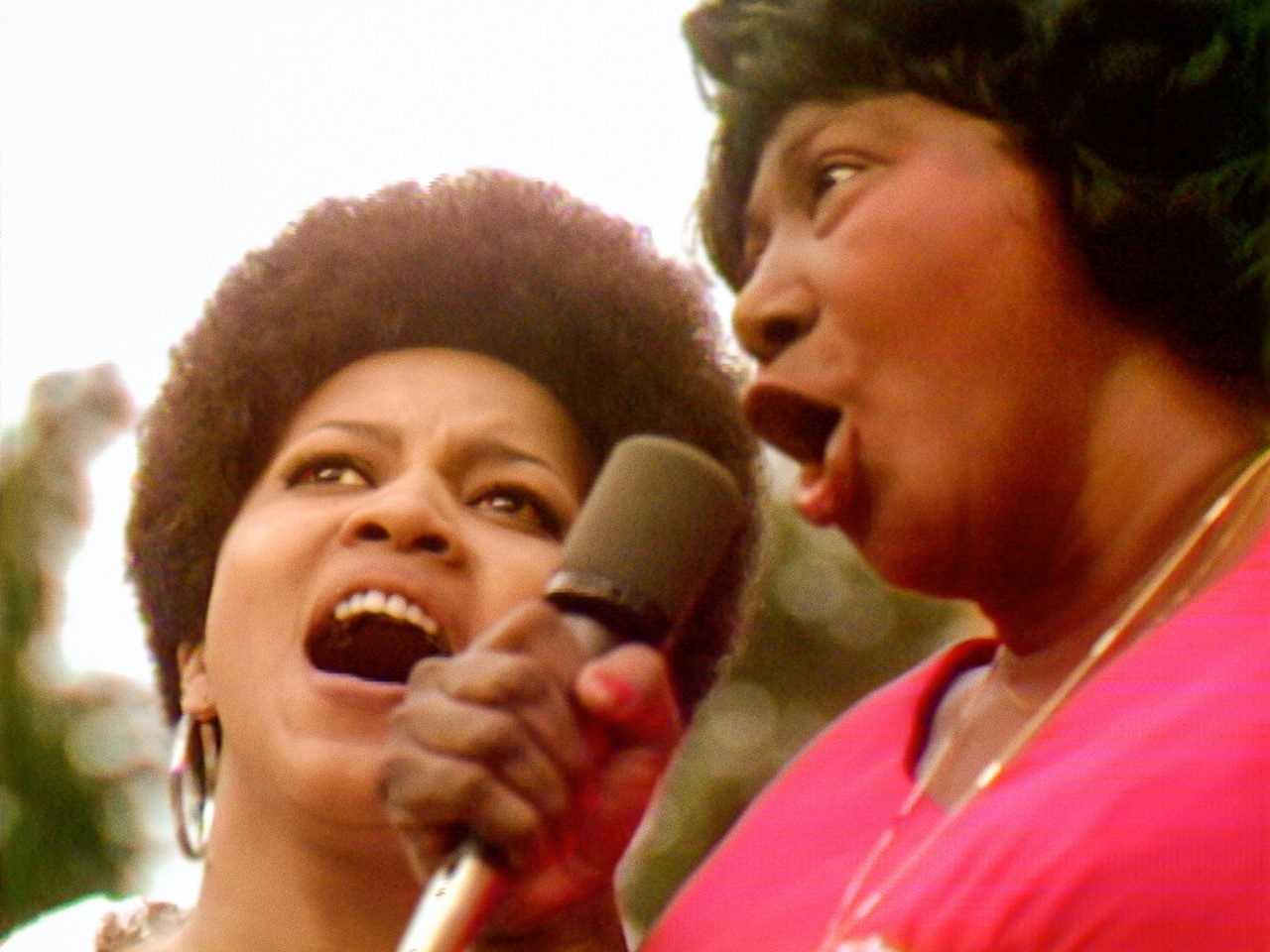 Two black women singing into a microphone