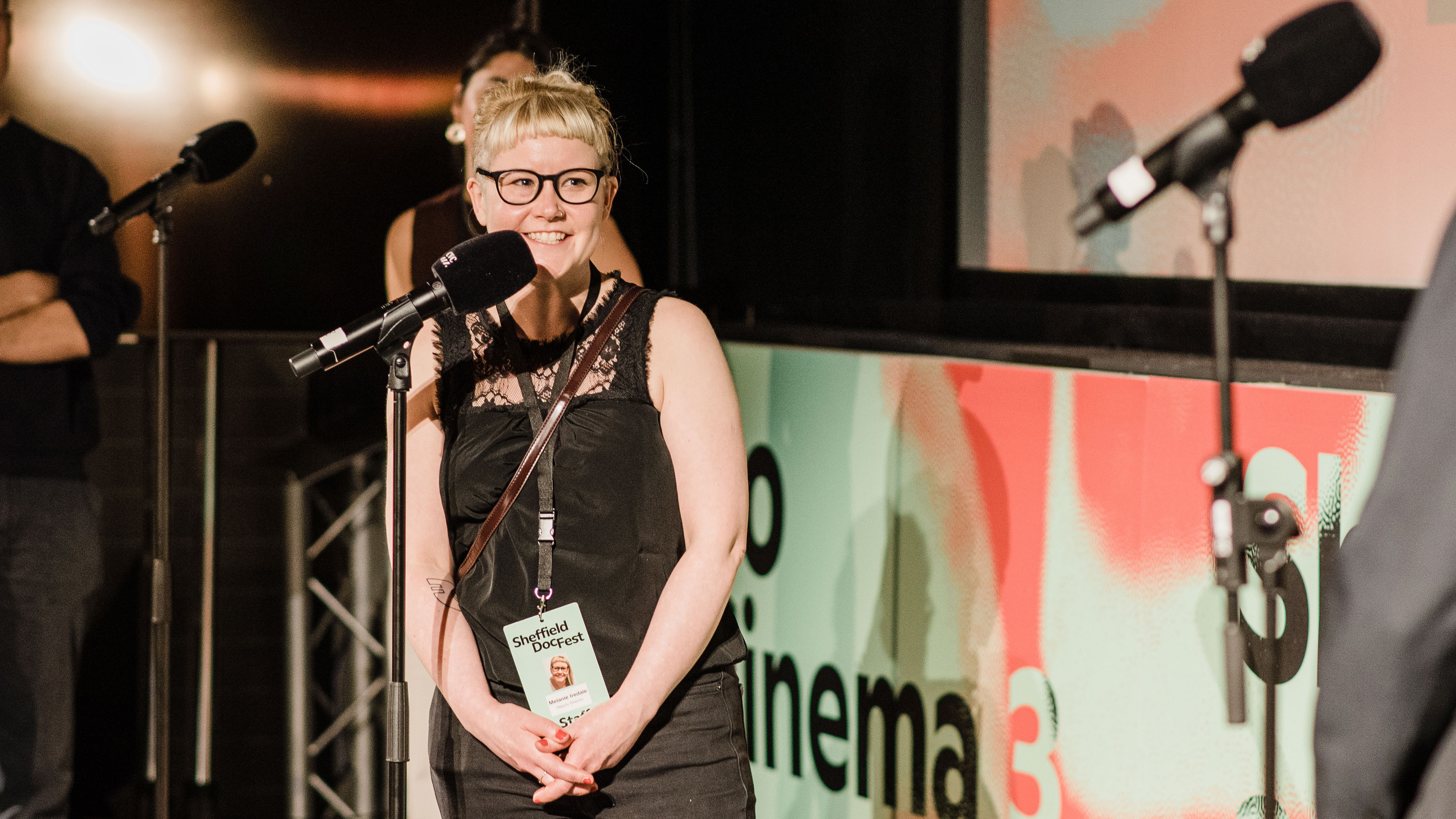 Woman smiles towards the camera whilst stood in front of a microphone.