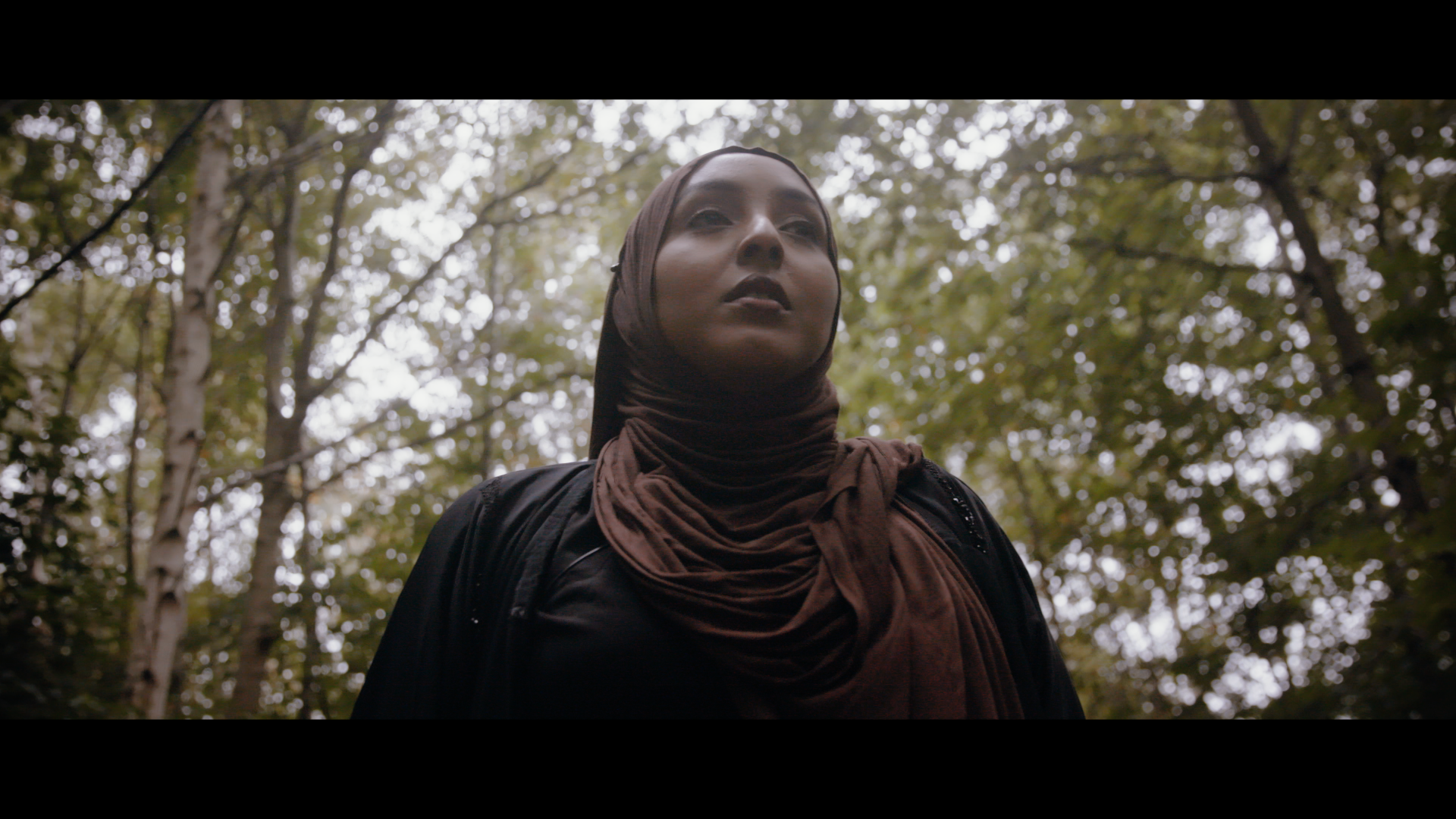 A woman wearing a headscarf is pictured centrally in the frame surrounded by trees