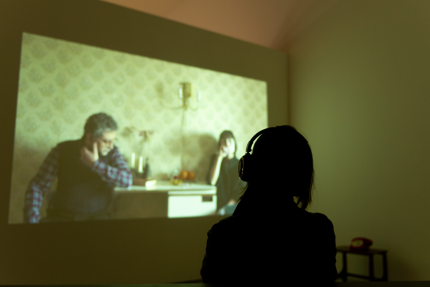 Silhouette of a person wearing headphones, sat in front of a video projection.