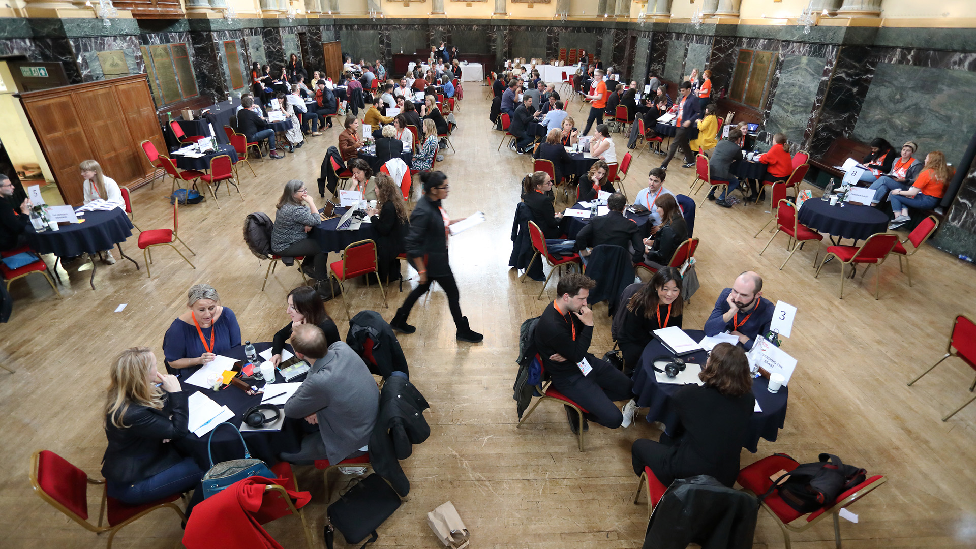 Aerial view of a grand hall. People sat in discussion around round tables.