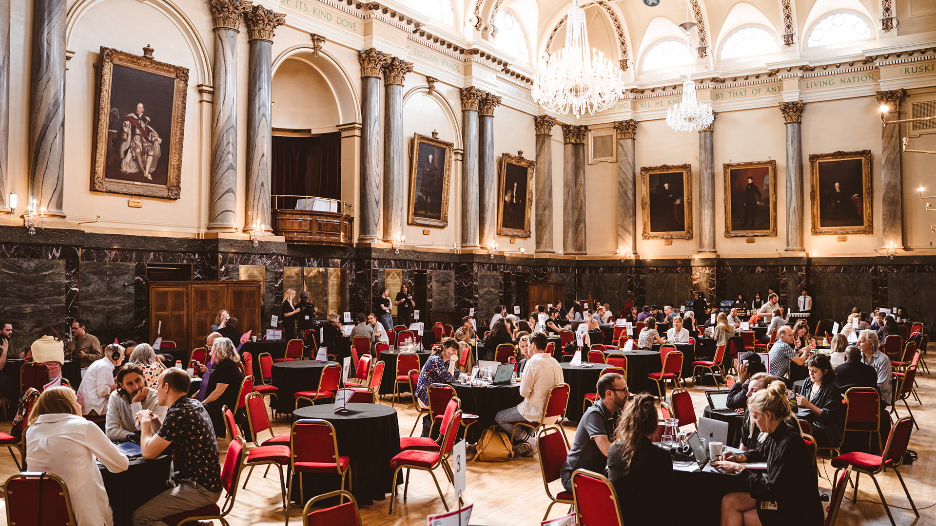 Groups of people sat at tables, in discussion, in a grand hall.