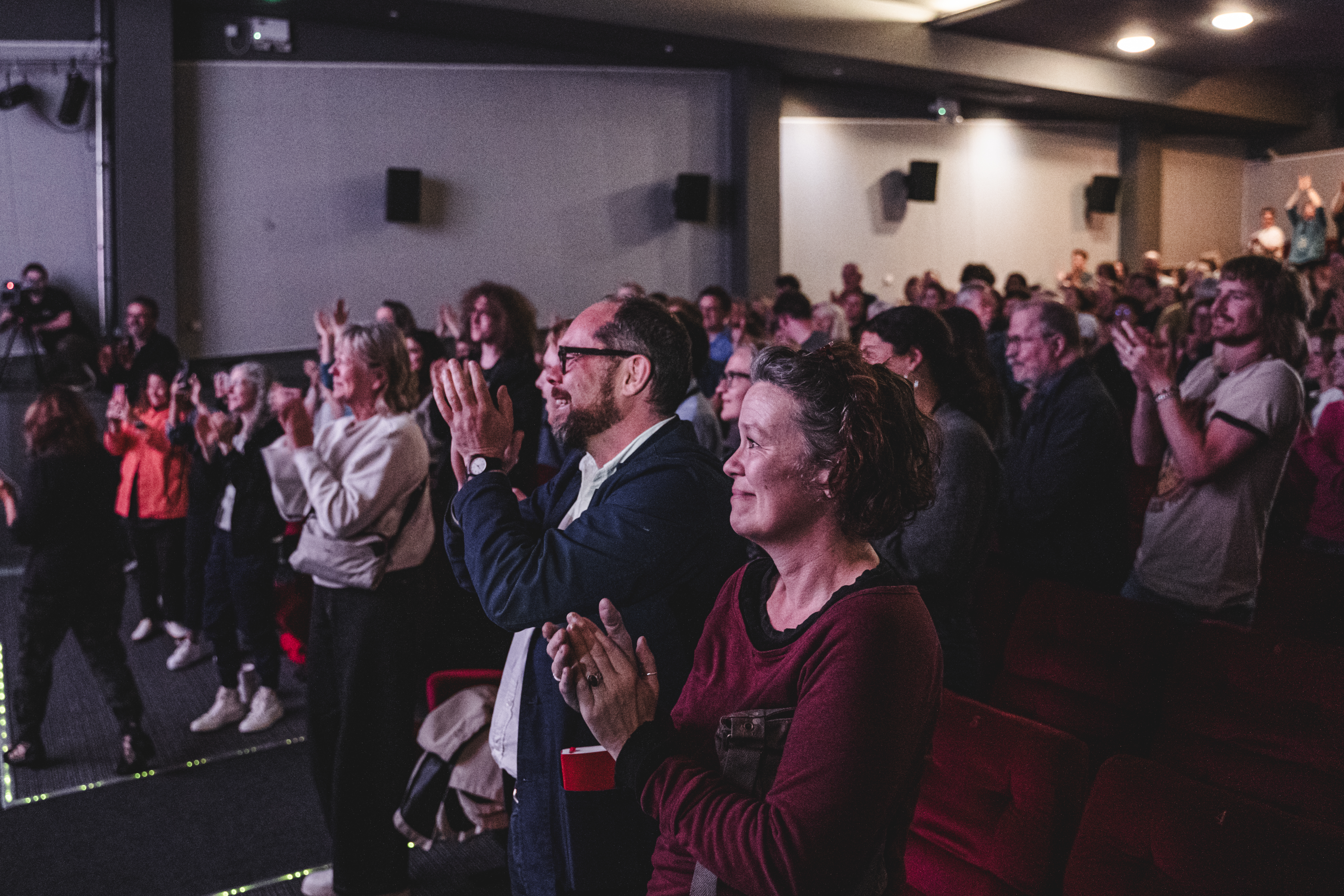 Busy crowd of people in a cinema screen clapping their hands and smiling. 