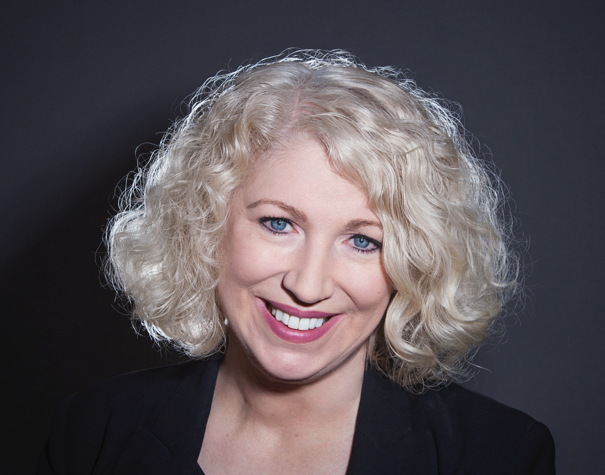 Headshot of Anne Morrison - head and shoulders of a woman with chin length curly hair smiles widely at the camera 