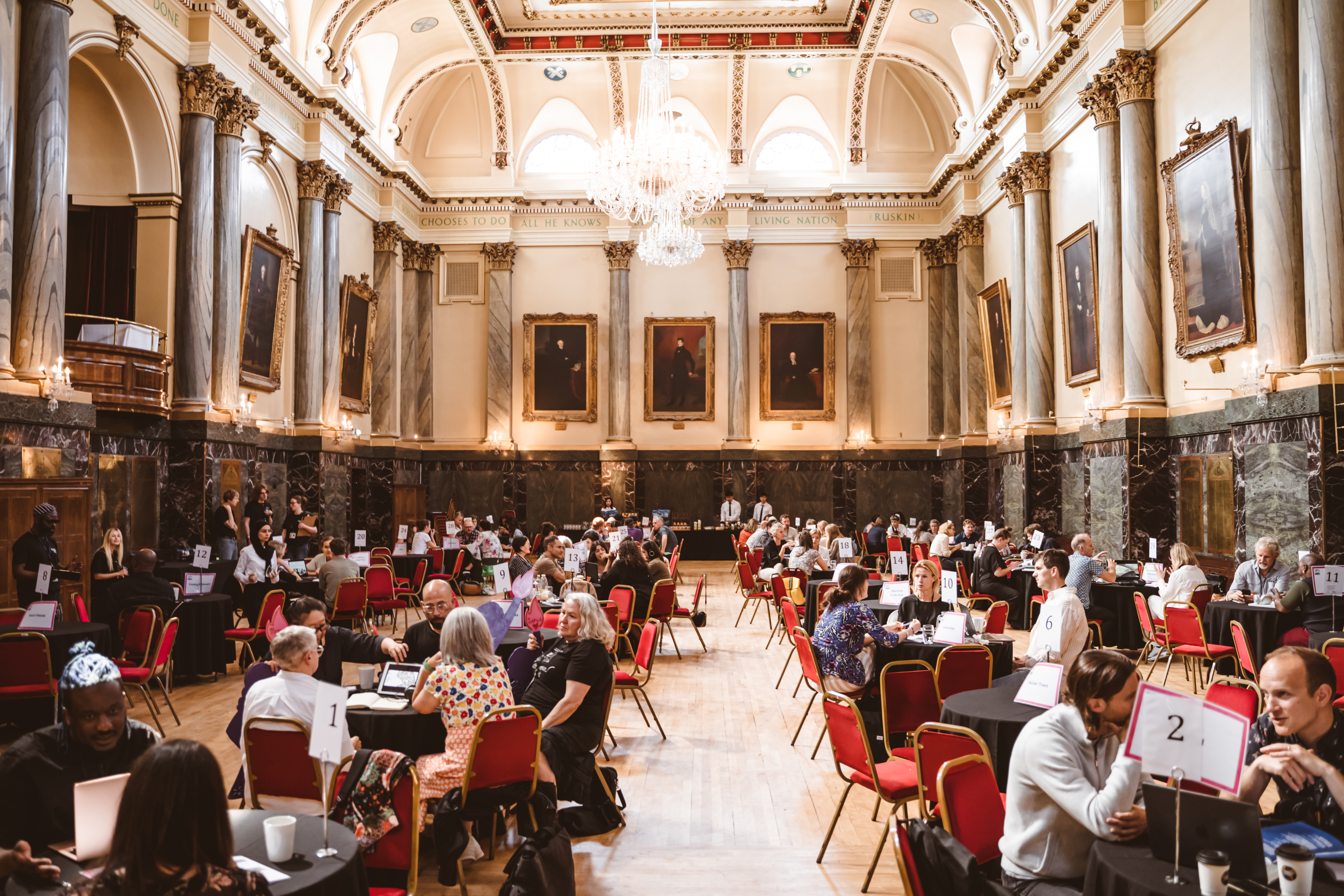 Groups of people sat at tables, in discussion, in a grand hall.