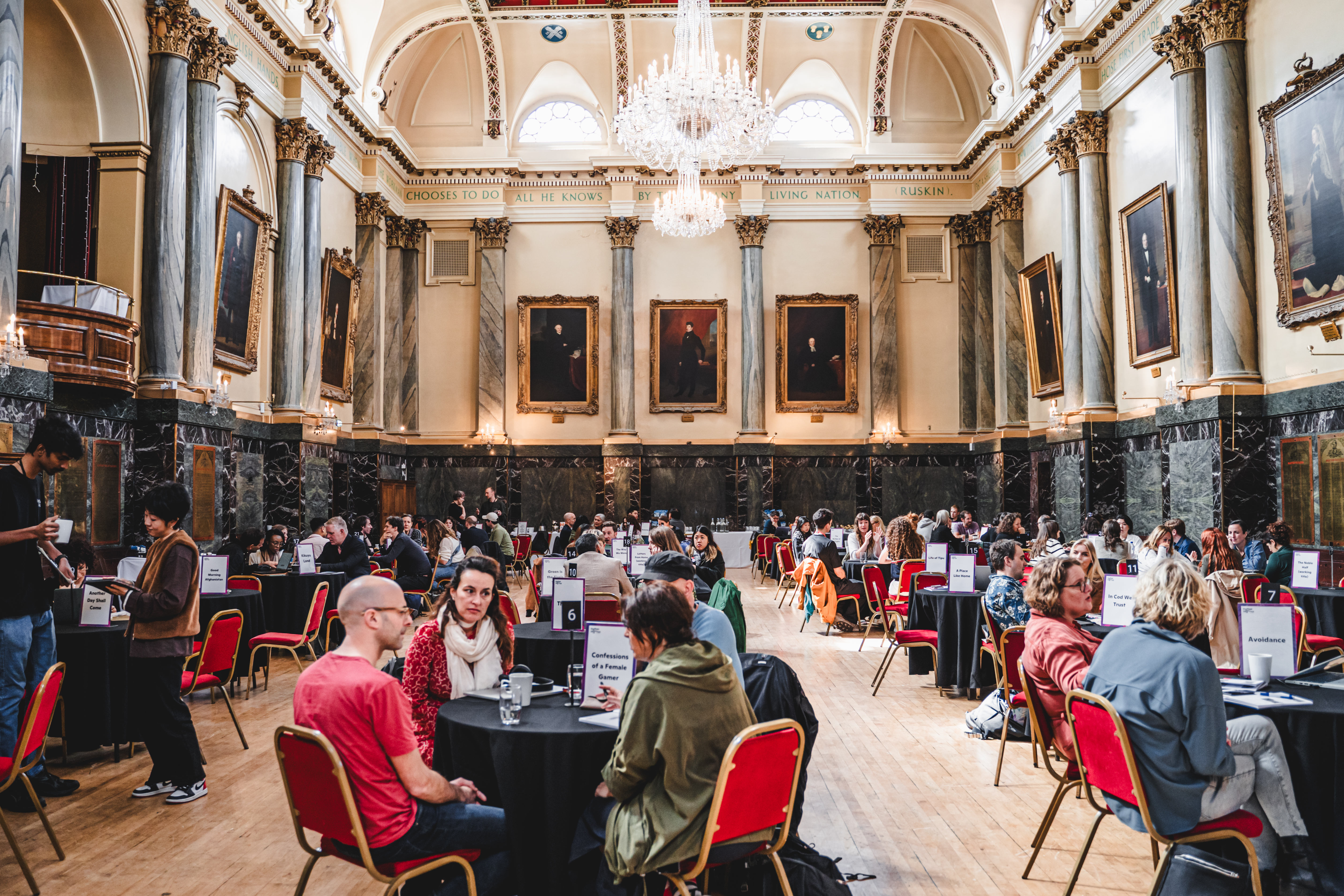 A photo of a large hall filled with groups of people holding meetings seated around small tables