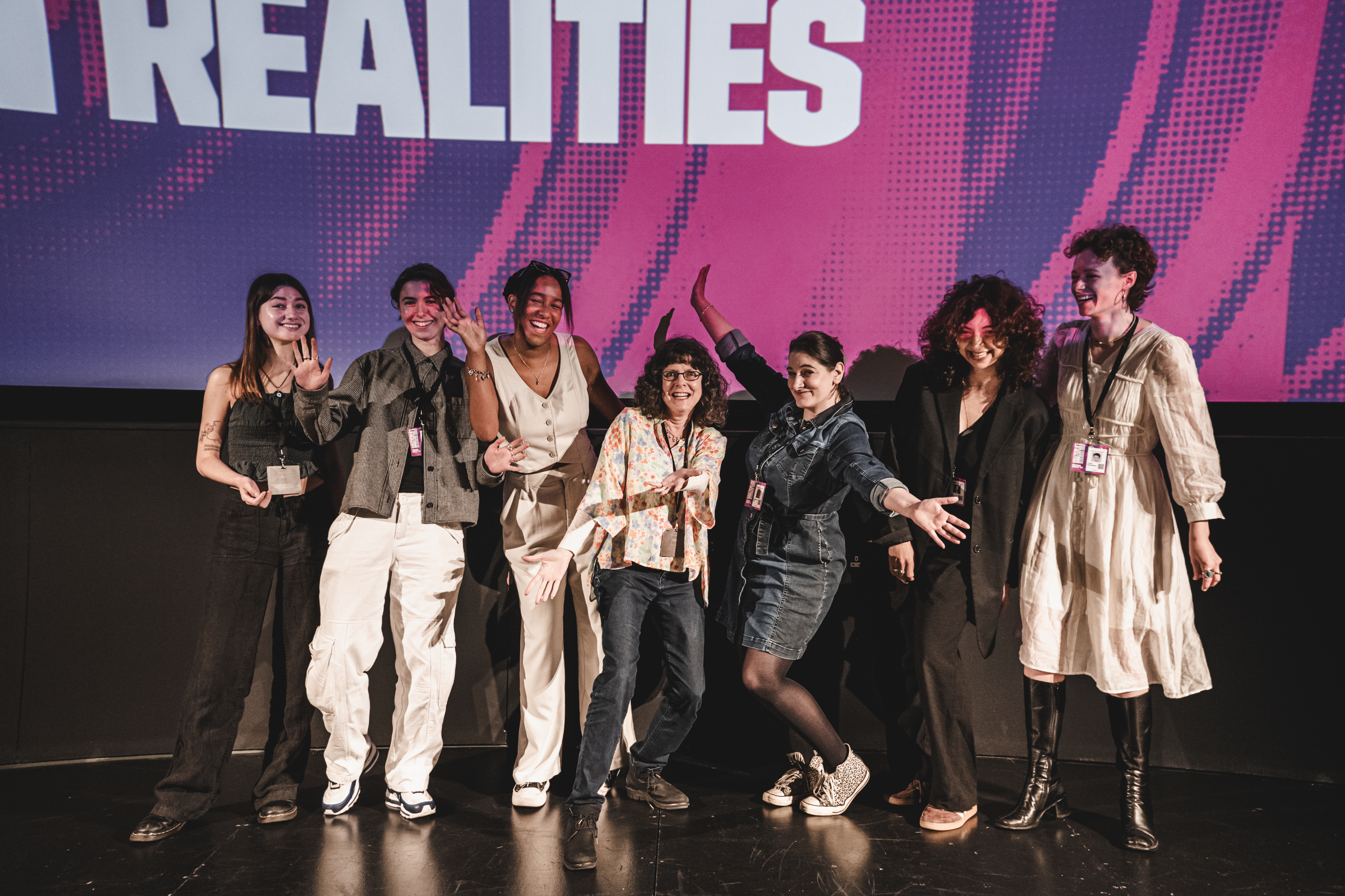 A group of people stood on a stage looking joyful, with smiles on their faces and their hands in the air.