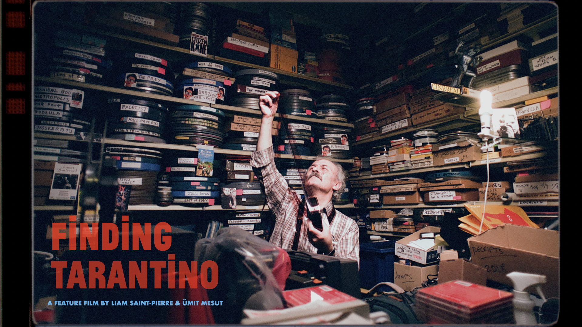 A man with grey hair examines a strip of film in a cluttered room filled floor-to-ceiling with labeled film reels, boxes, and VHS tapes.
