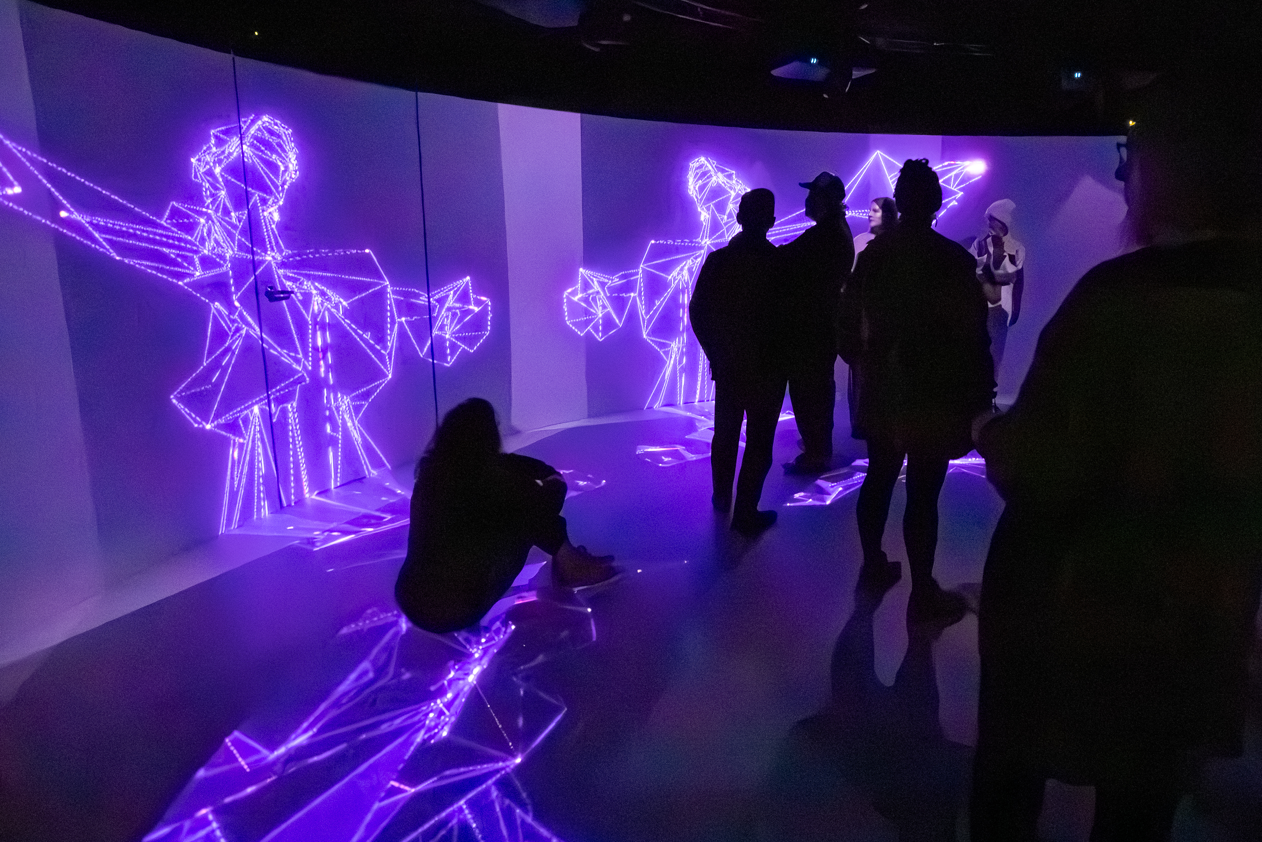 A group of people stand in front of a purple wall within an alternate realities exhibition.