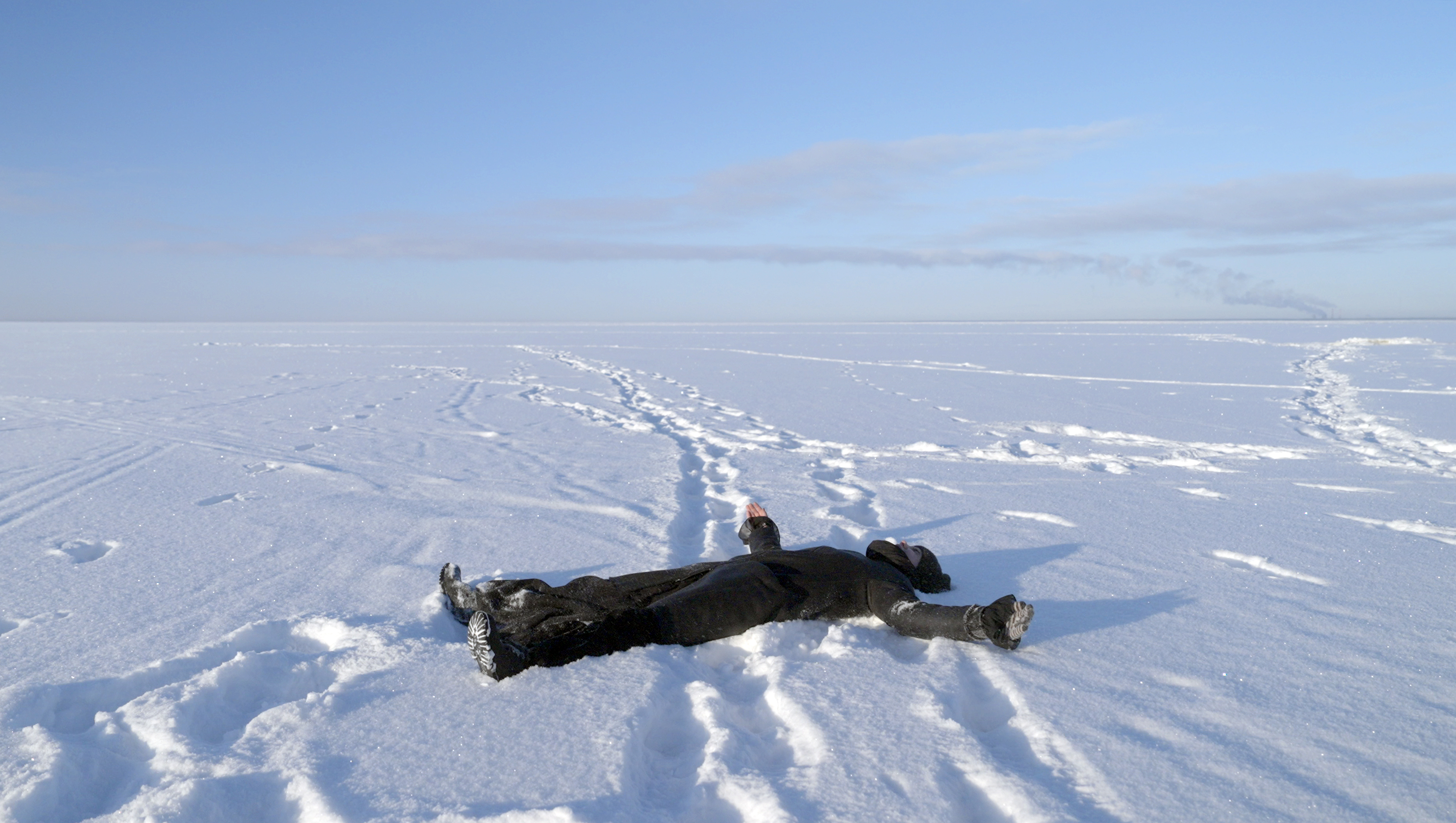 A person dressed in all black laid on their back in snow.