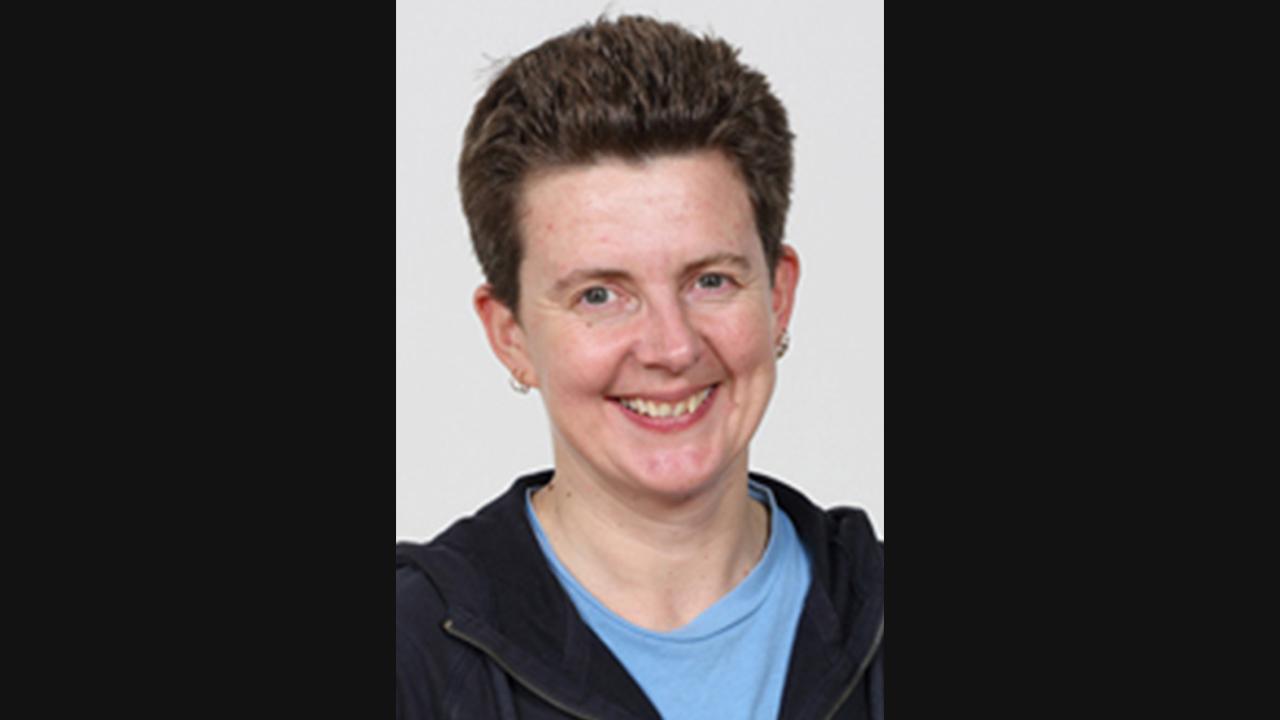 Fiona Outram headshot. Image of a white woman with short dark brown hair. She is wearing a blue t shirt and black hoodie.