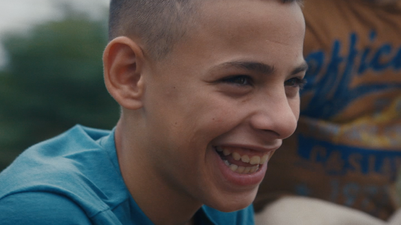 An image of a young boy smiling. He's wearing a blue t-shirt.