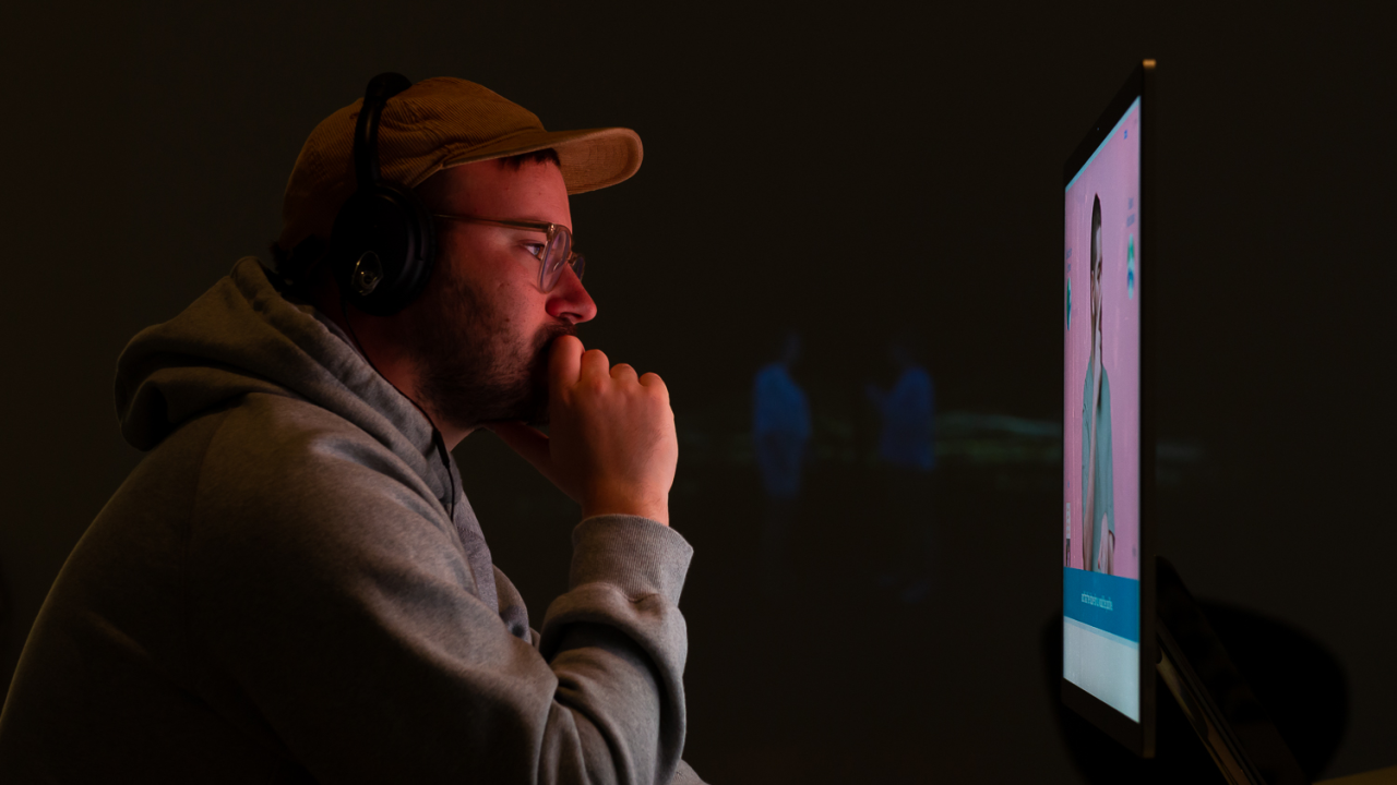 A man watches a screen with a cap and headphones in a dark room.