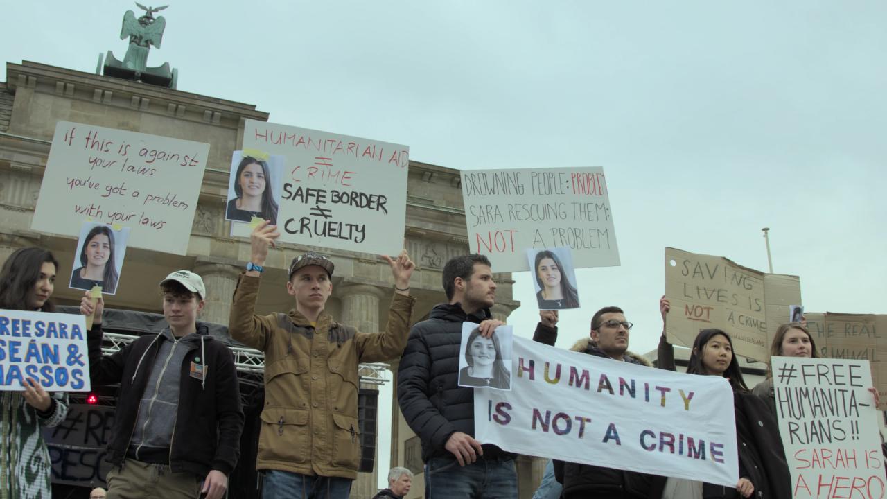 People standing with signs, some of which read 'Humanity is not a Crime'