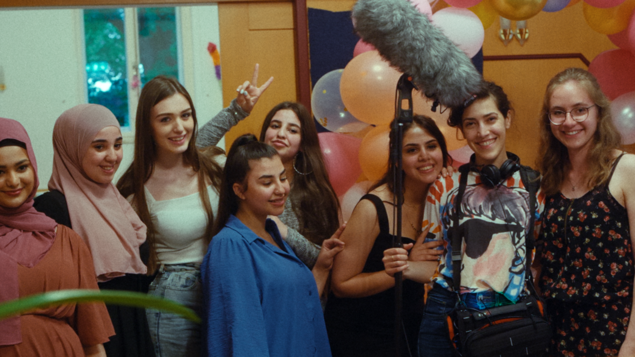 A group of teenage girls stand in a line, smiling widely at the camera