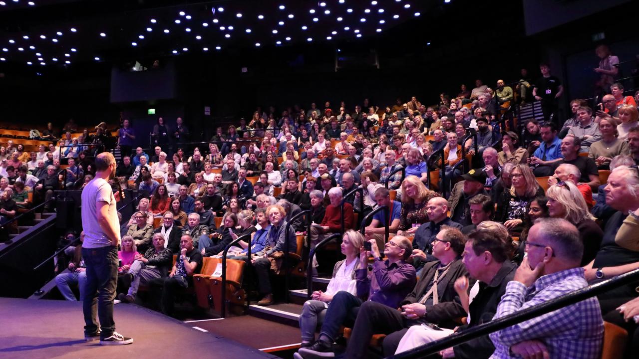 Large crows of people sat in a theatre in-the-round