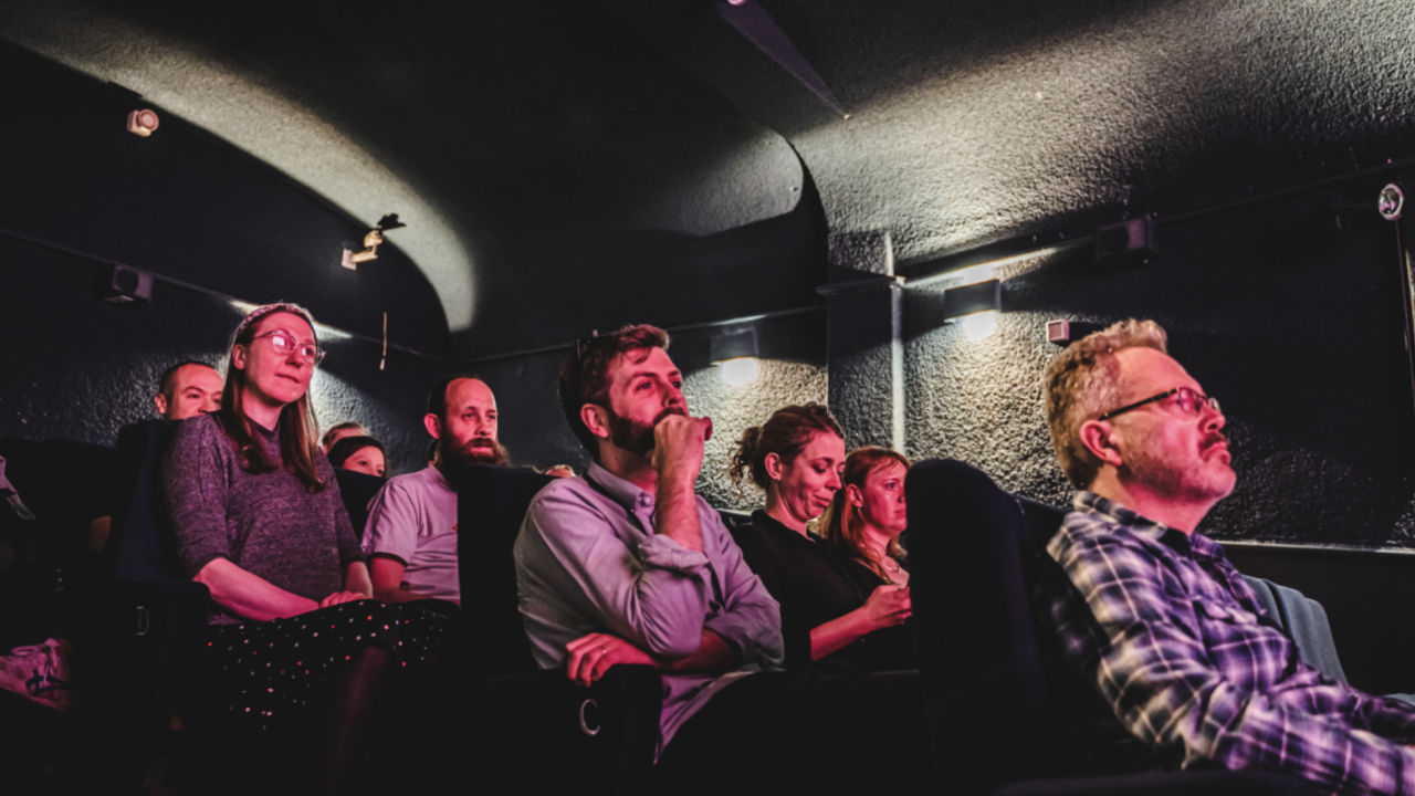 A crowd of people in a small cinema concentrate on the screen in front of them.