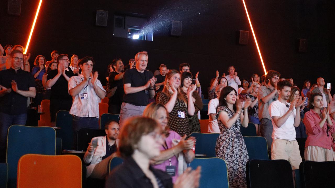 A busy cinema crowd stands to a round of applause.