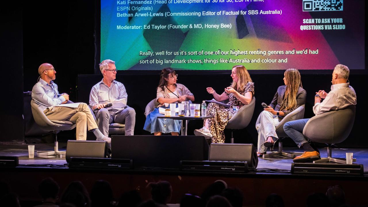 Five people sit on chairs on a stage engaged in conversation.
