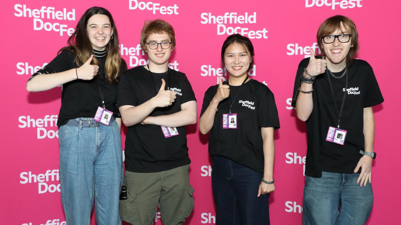 Four young people stand in front of a pink step and repeat in black DocCrew t-shirts.