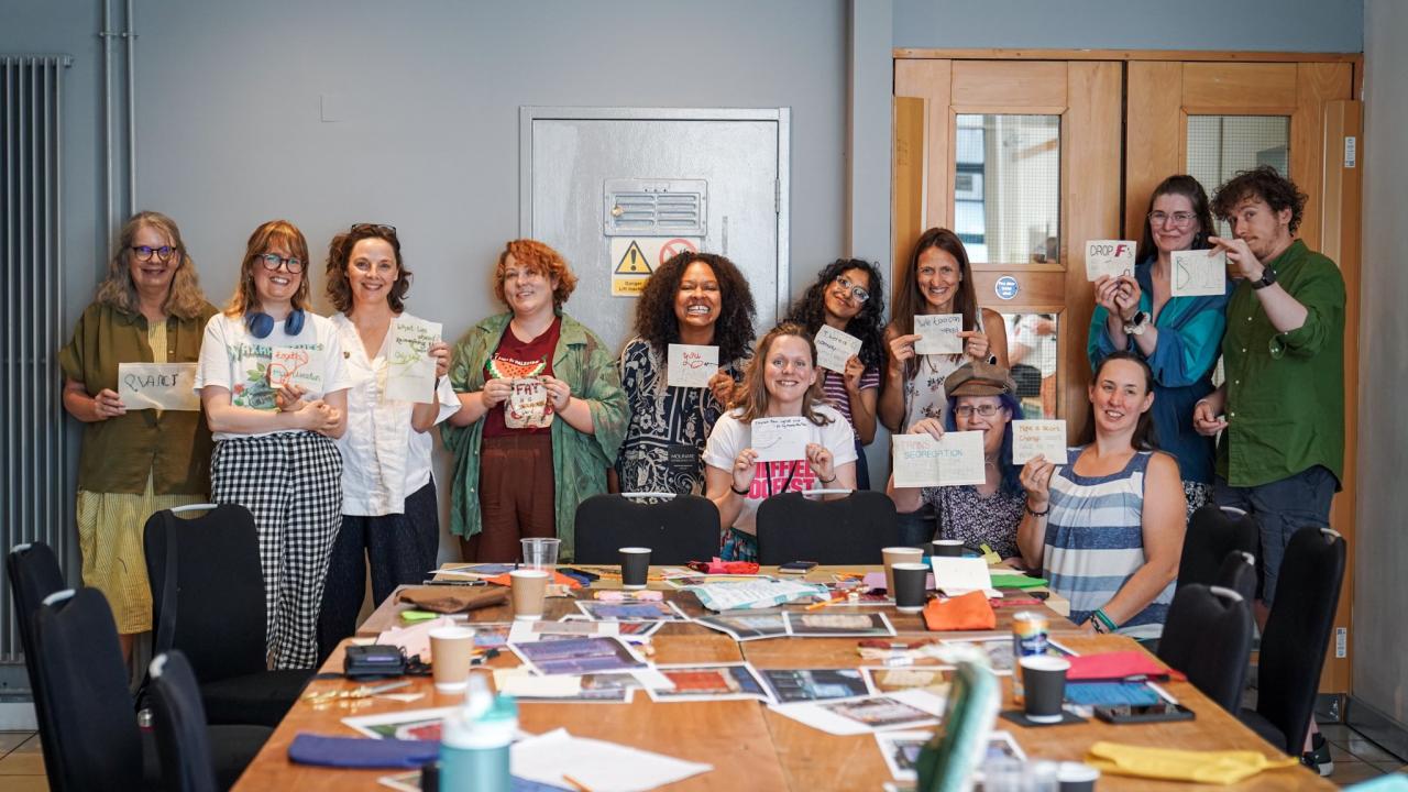 A group of people stand around a table holding pieces of art they have created. They have wide smiles on their faces. 