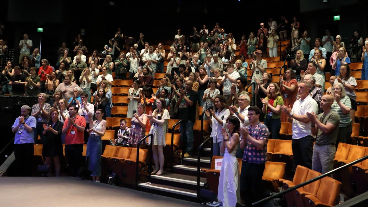 An audience at a DocFest event stand and applaud at the end.