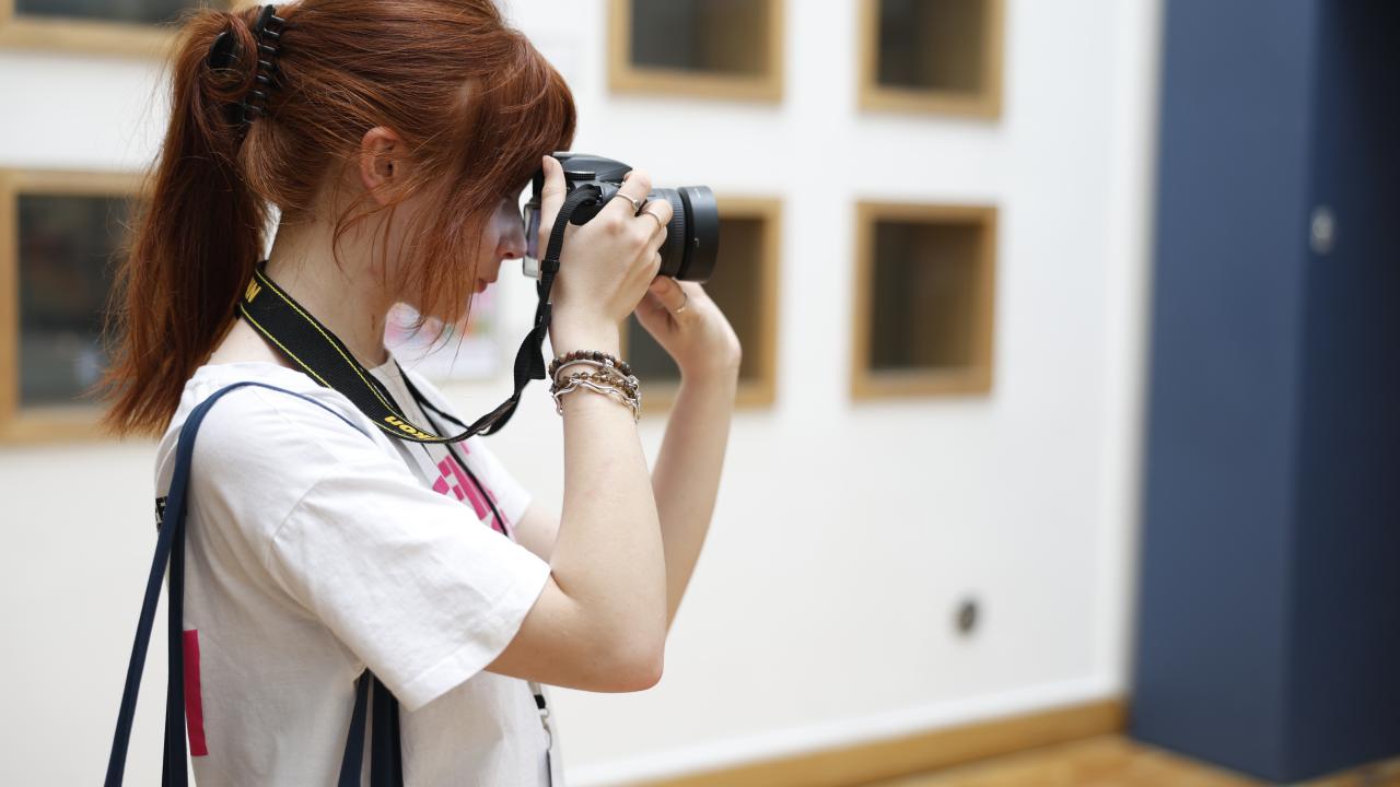 A girl holds a camera whilst working as a volunteer at a festival.