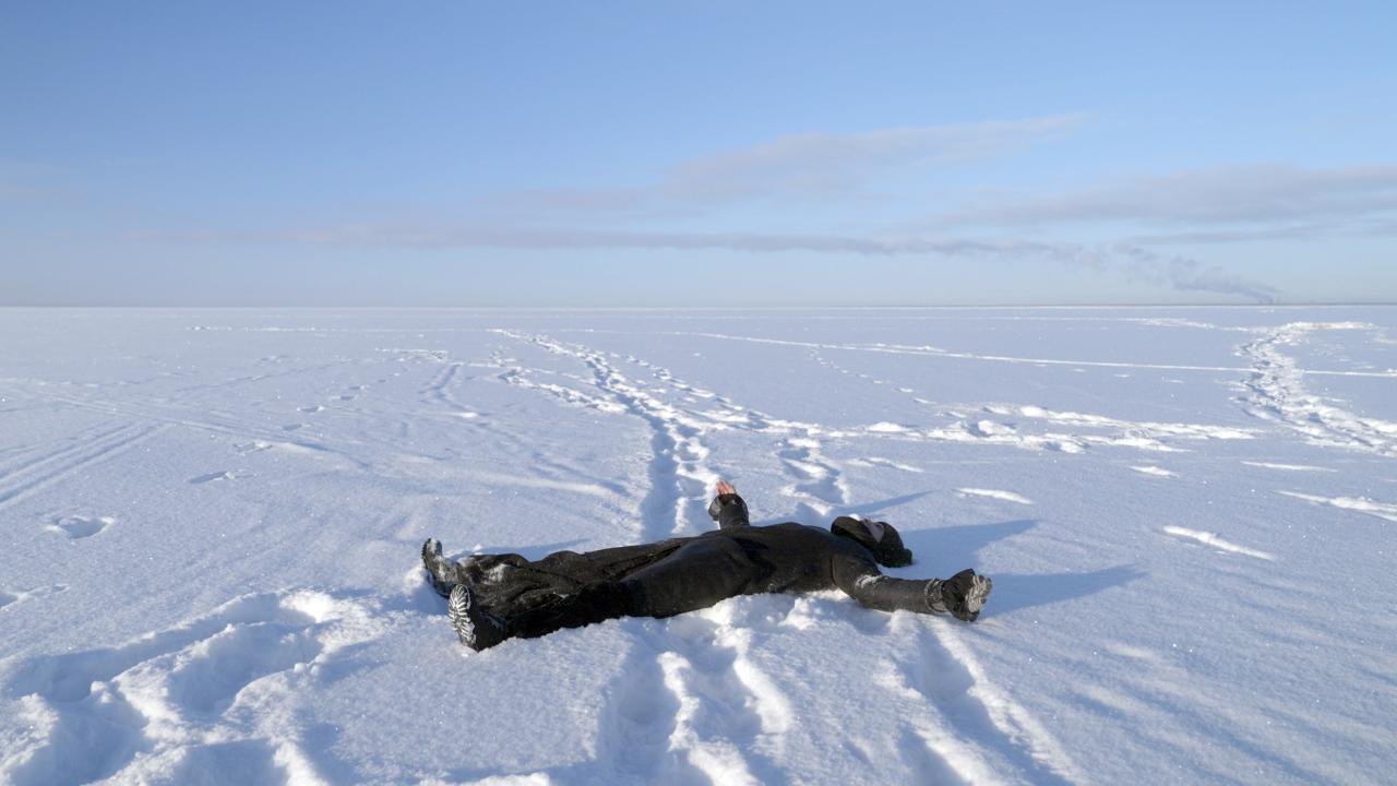 A person dressed in all black laid on their back in snow.