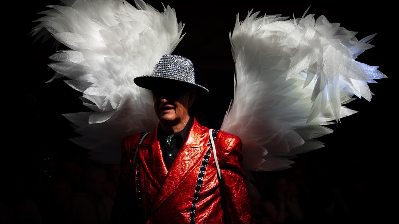 A still from the film Heaven 17: The Last Temptation. A man in a red jacket stands in a costume with big wings.