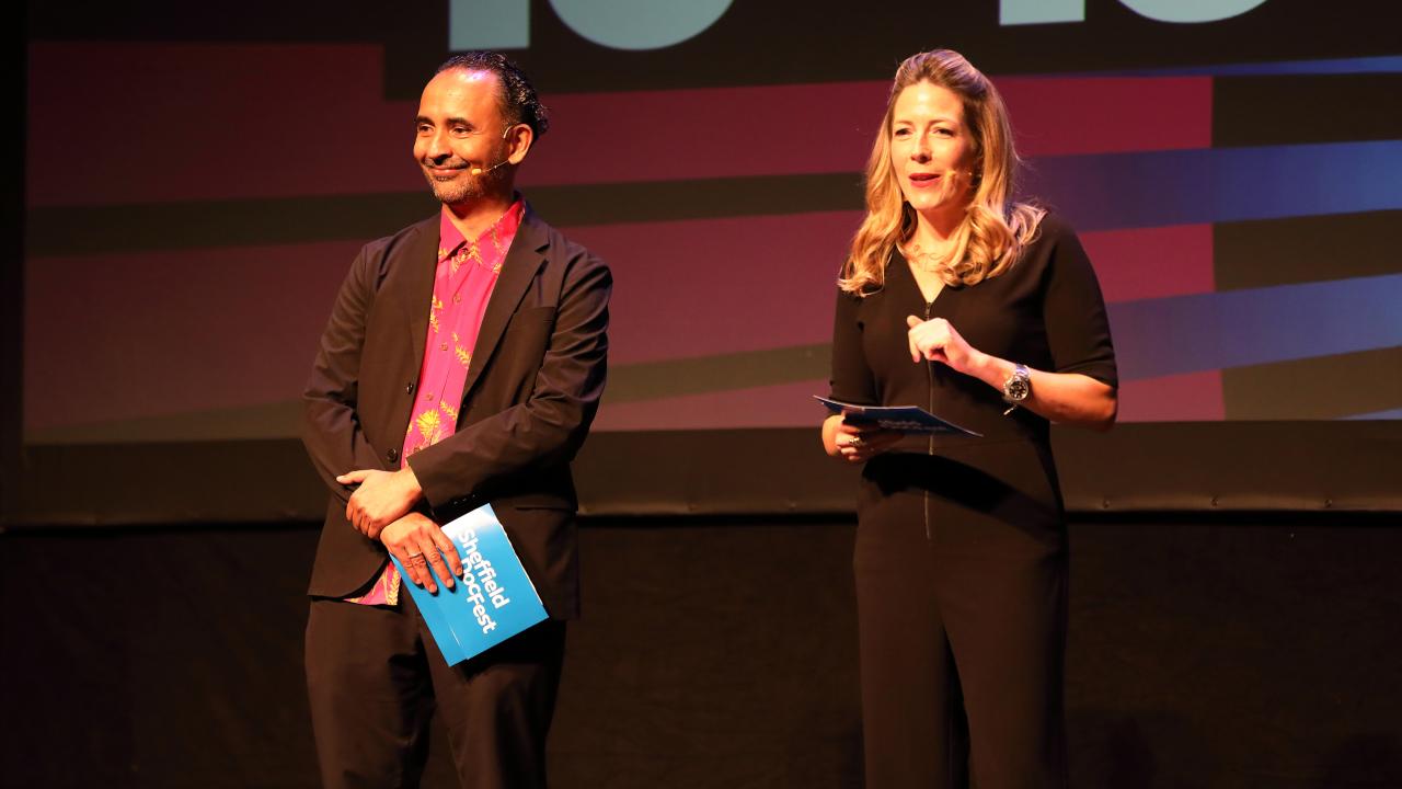 A man wearing a blazer and red shirt, and a woman wearing a black top and trousers present at Sheffield DocFest.