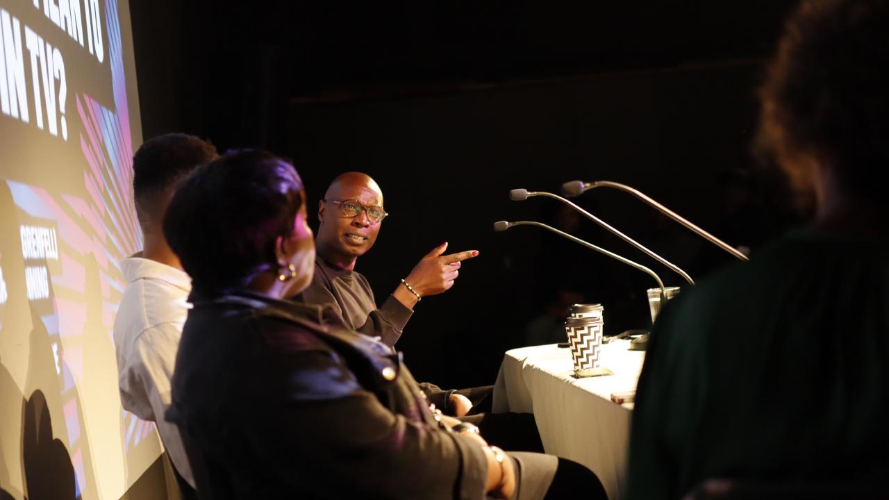 A panel of people discuss in front of a slide graphic.