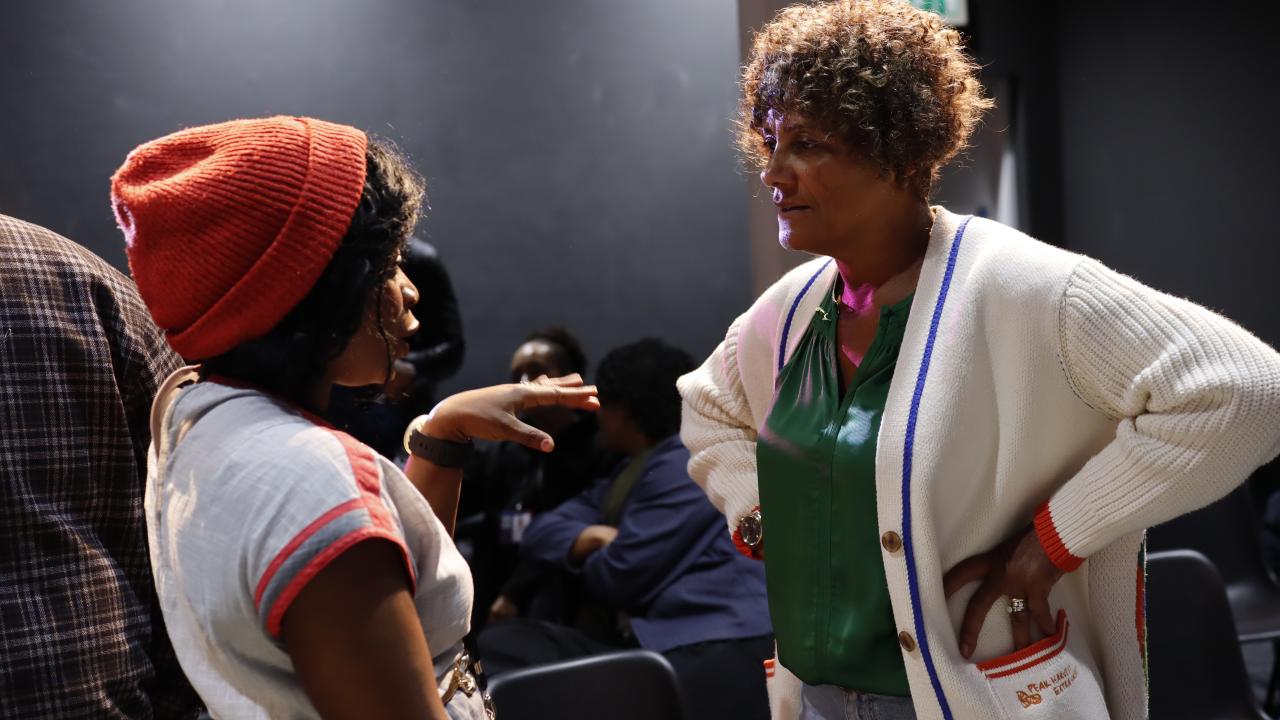 A woman in an orange hat talks to a woman with her hands on her hips.