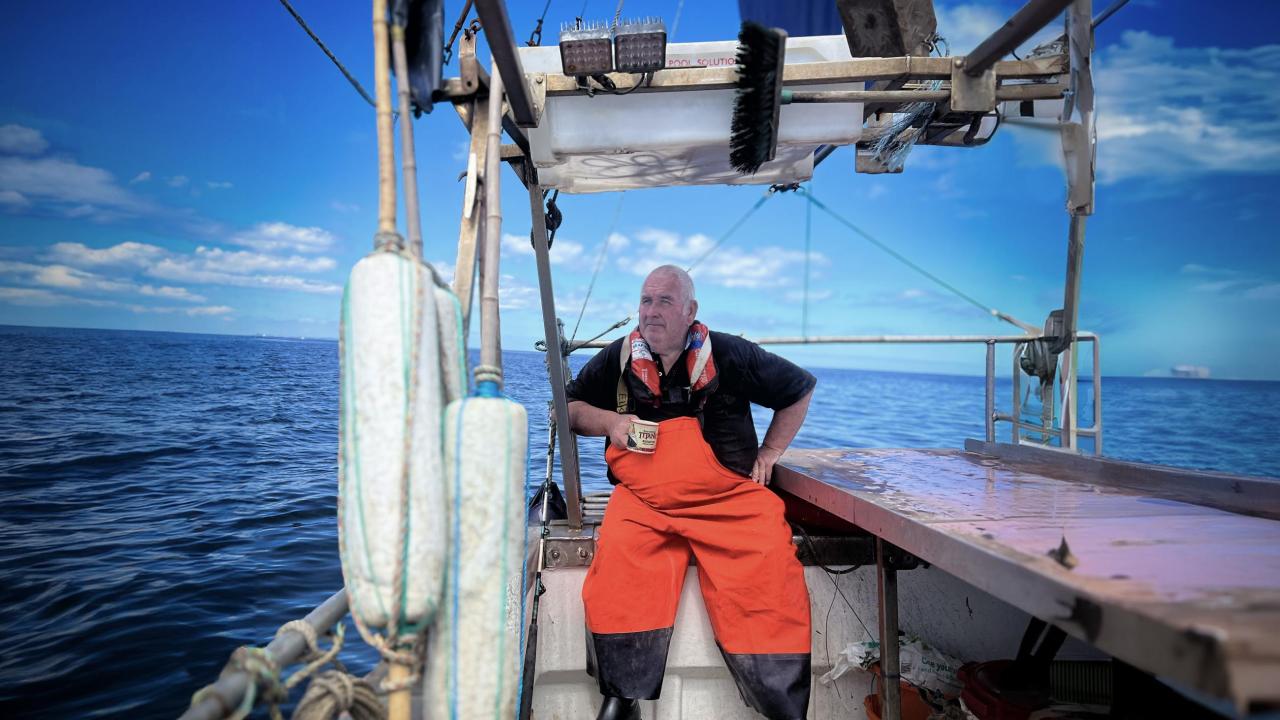 A fisherman in orange overalls, sitting on a boat, out at sea
