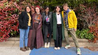 Sheffield DocFest 2023 Youth Jurors Jenny Luisa Barruol, Alexandra Judkins, Amanda Daud, Annabel Bai Jackson, and Tymofii Donets stood next to each other in front of some red and green foliage