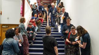 Queues of people stood either side of a staircase in a cinema, talking and having their tickets checked.