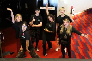 Six volunteers wearing black t-shirts with their hands in the air