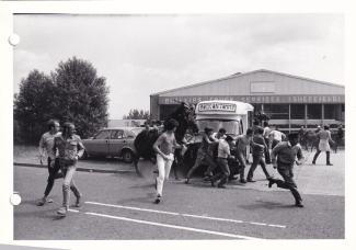 Black and white photo of a confrontation between people and police in front of an ice cream van at Orgreave during the Miners' Strike