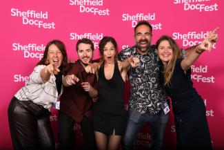 Five people point at a camera with wide smiles on their faces.